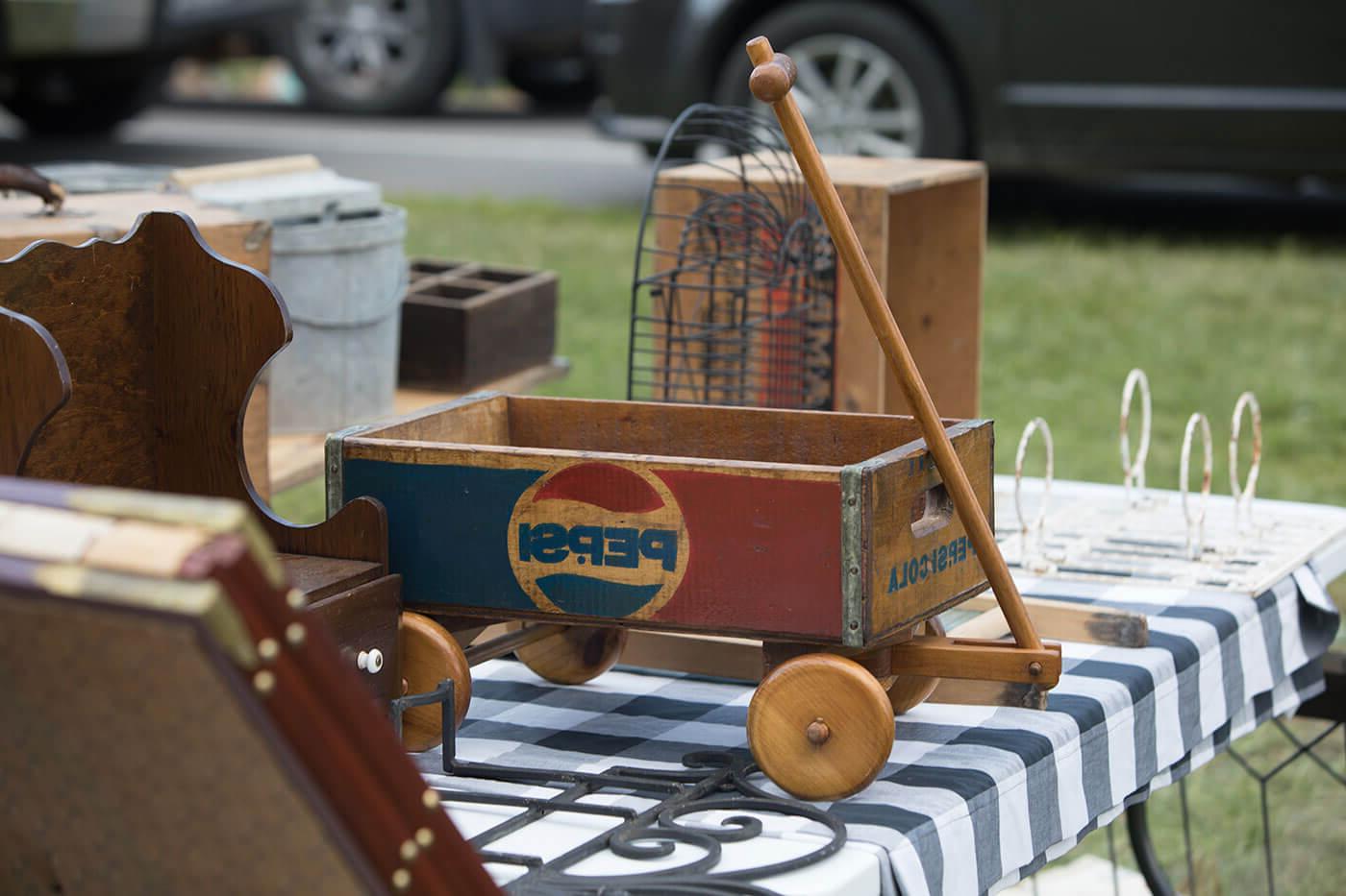 An old wooden wagon with the Pepsi logo painted on it sits on a checkered tablecloth.